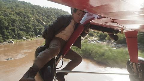 Tom Cruise klammert sich an ein fliegendes, rotes Propellerflugzeug. Er blickt angespannt nach vorne. - Foto: Paramount Pictures