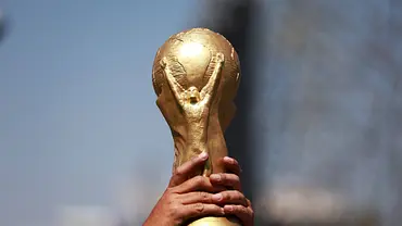 Eine Person hält die goldene FIFA-Weltmeisterschaftstrophäe mit beiden Händen in die Höhe, vor unscharfem Hintergrund. - Foto: IMAGO / Anadolu Agency