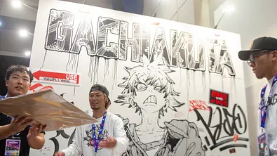 Hideyoshi Andou steht vor einer großen „Gachiakuta“-Graffitiwand mit einer gezeichneten Figur auf der San Diego Comic-Con 2026. - Foto: IMAGO / MediaPunch
