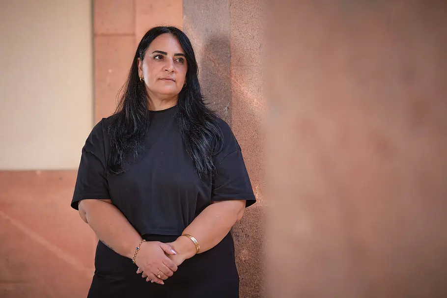 Gamze Kubaşık Gamze Kubaşık steht in schwarzer Kleidung mit gefalteten Händen vor einer rötlichen Steinwand und blickt zur Seite.