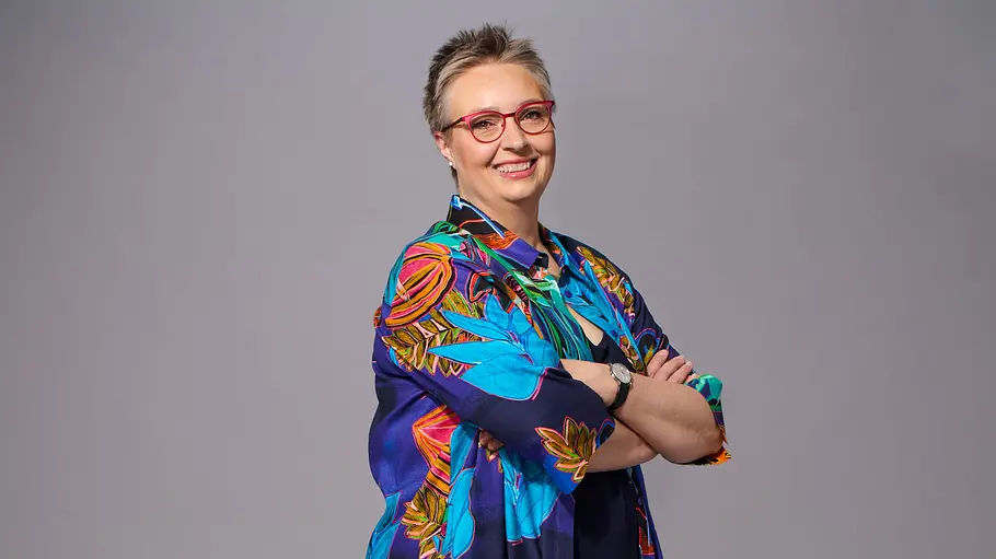 Adrianne Rickel trägt ein buntes Oberteil und lächelt freundlich in die Kamera.