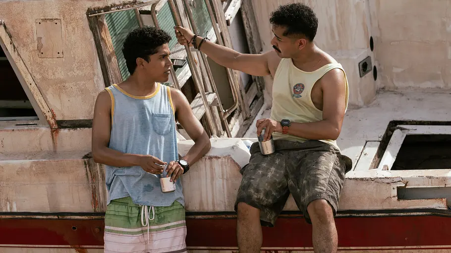 „Gegen den Hurrikan“ hält sich wacker an der Spitze der Netflix-Charts. Wirpul und Candi in Shorts und ärmellosen Shirts halten Dosen an einem verwitterten Boot. Candi sitzt auf der Bordwand.