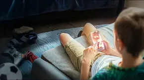 Generation Porno - Was unsere Kinder online sehen: Ein Junge sitzt im Anschnitt mit dem Rücken zur Kamera auf seinem Bett und schaut auf sein Smartphone. Auf dem Display ist undeutlich eine Frau in Unterwäsche abgebildet. - Foto: ZDF und getty