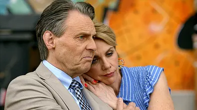 Yvonne im blau-weiß gestreiften Oberteil lehnt ihren Kopf an Gerners Schulter. Er trägt einen beigen Anzug und blickt ernst. - Foto: RTL