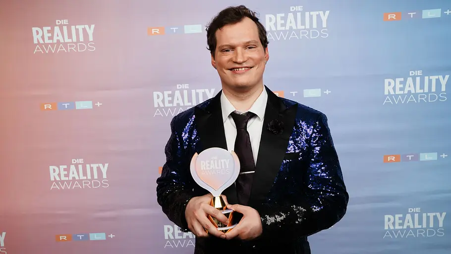 Fritz Wagner bei den Reality Awards Fritz mit Reality Award in den Händen vor der Fotowand der Reality Awards.