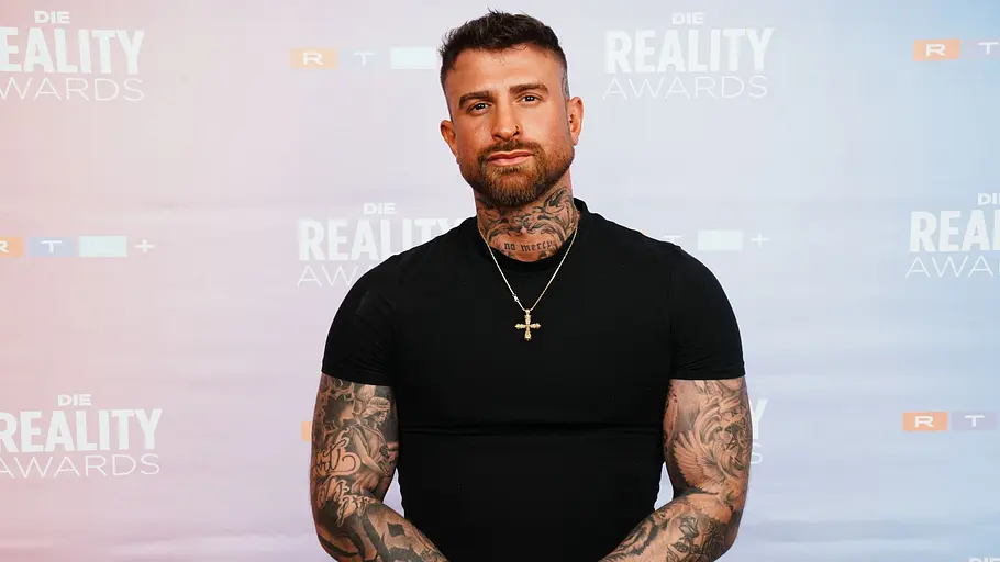 Gigi bei den Reality Awards Gigi mit schwarzem T‑Shirt posiert vor der „Die Reality Awards“-Fotowand.