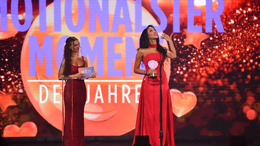 Vanessa Nwattu bei den Reality Awards Zwei Frauen in roten Kleidern stehen auf einer Bühne bei einer Preisverleihung.