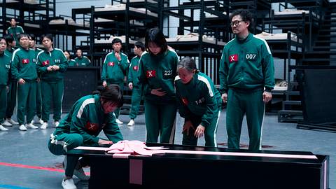 Vier Spieler*innen stehen vor einer großen, schwarzen Box, die mit einer rosa Schleife geschmückt ist. - Foto: Noh Ju-han / Netflix