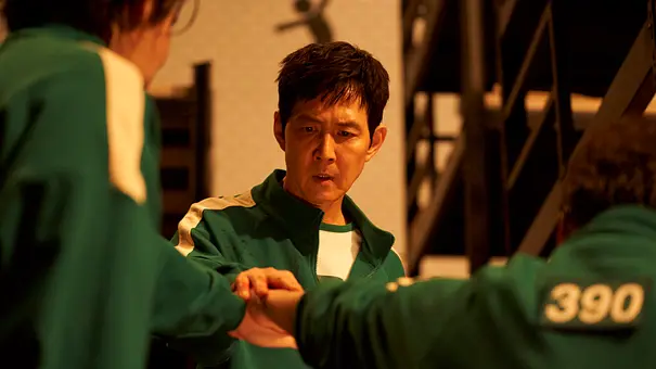 Gi-hun legt seine rechte Hand auf die Hände von zwei anderen Spielern. - Foto: No Ju-han/Netflix Gi-hun legt seine rechte Hand auf die Hände von zwei anderen Spielern. - Foto: No Ju-han/Netflix