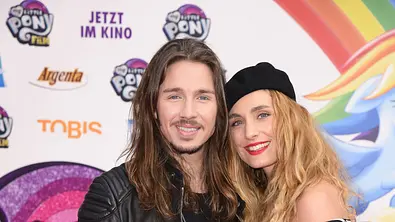 Gil Ofarim und seine damalige Ehefrau Verena posieren Arm in Arm bei einer Filmpremiere vor einer bunten Fotowand. - Foto: IMAGO / Gartner