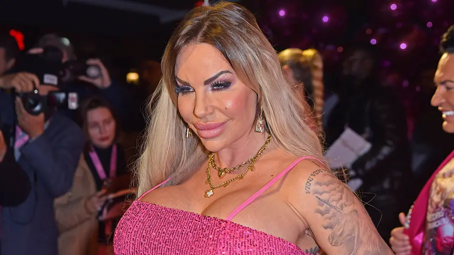 Gina-Lisa Lohfink 2023 Gina-Lisa im pinkfarbenen Kleid mit Schmuck steht bei einer Abendveranstaltung, Fotografen im Hintergrund.