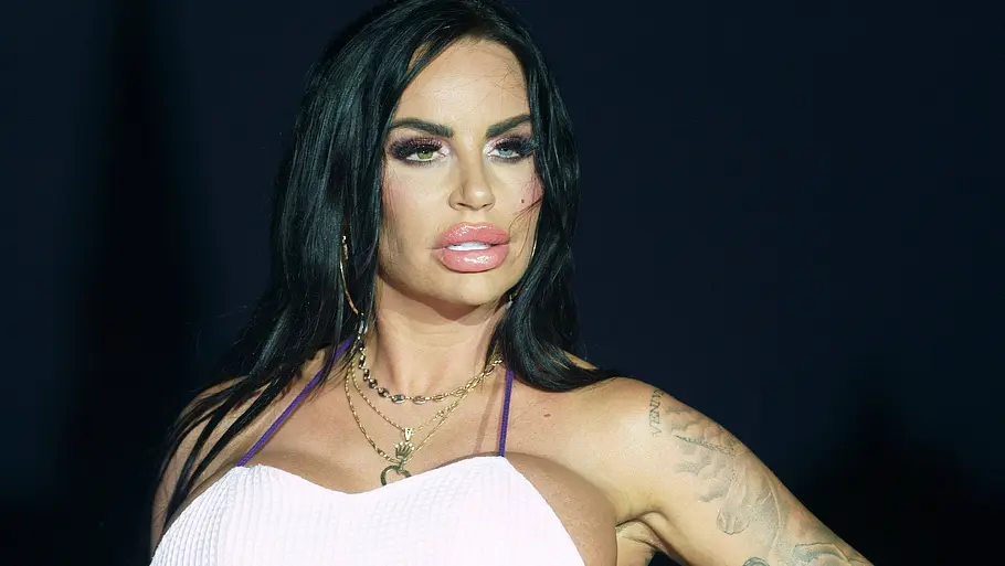 Gina-Lisa in 2022 Gina-Lisa mit langen dunklen Haaren und tätowierten Armen posiert in einem hellrosa Kleid auf einem Laufsteg.