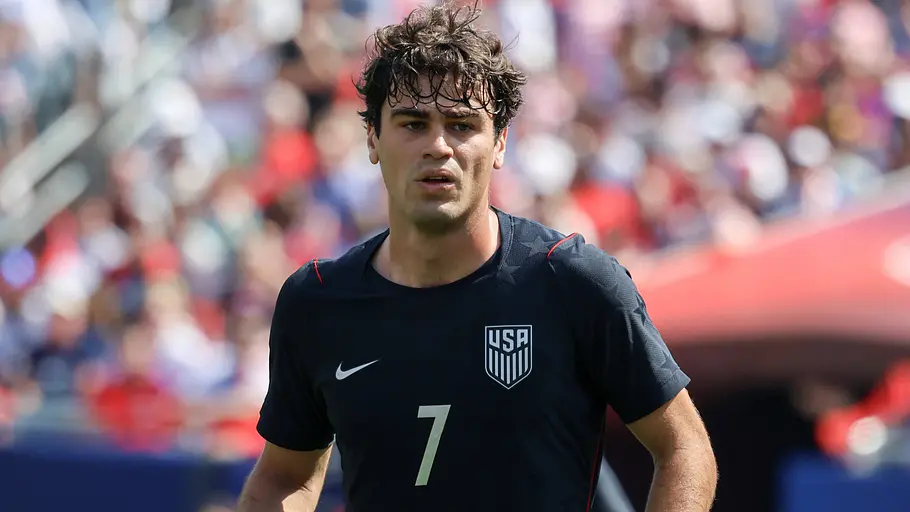 Ein US-amerikanischer Fußballspieler im dunkelblauen Nationaltrikot mit der Rückennummer 7 läuft während des Aufwärmens über den Rasen. Im Hintergrund sind die unscharfen Zuschauerränge eines voll besetzten Stadions zu sehen.