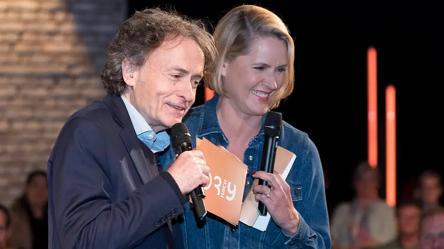 Giovanni di Lorenzo und Judith Rakers bei „3nach9“ Giovanni di Lorenzo und Judith Rakers stehen mit Mikrofonen und Moderationskarten im „3nach9“-Studio.