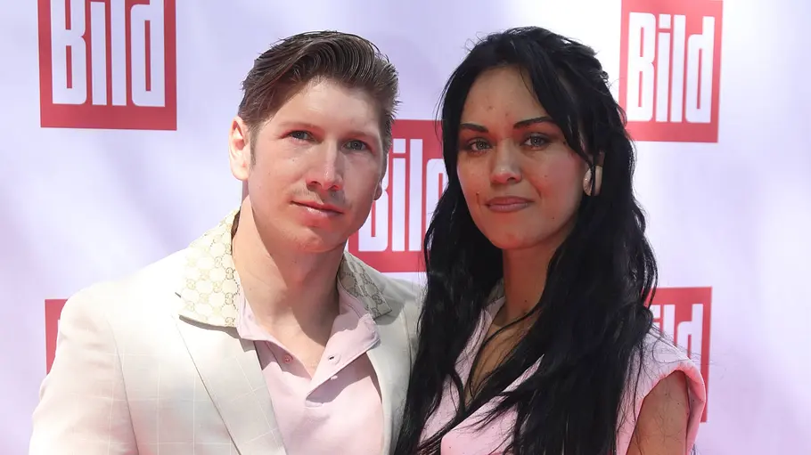 Giovanni Weisheit steht gemeinsam mit Vanessa Neigert vor einer Pressewand und blickt in die Kamera.