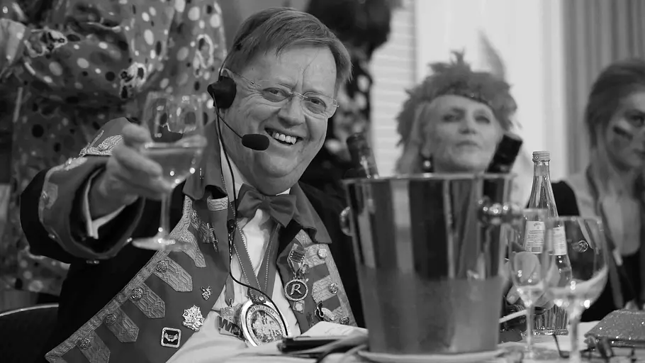 Gisbert Baltes war viele Jahre lang ein fester Bestandteil des Kölner Karnevals. Gisbert Baltes lächelt mit Headset und ordenbesetzter Jacke und hebt ein Weinglas. Die Aufnahme ist schwarz-weiß.