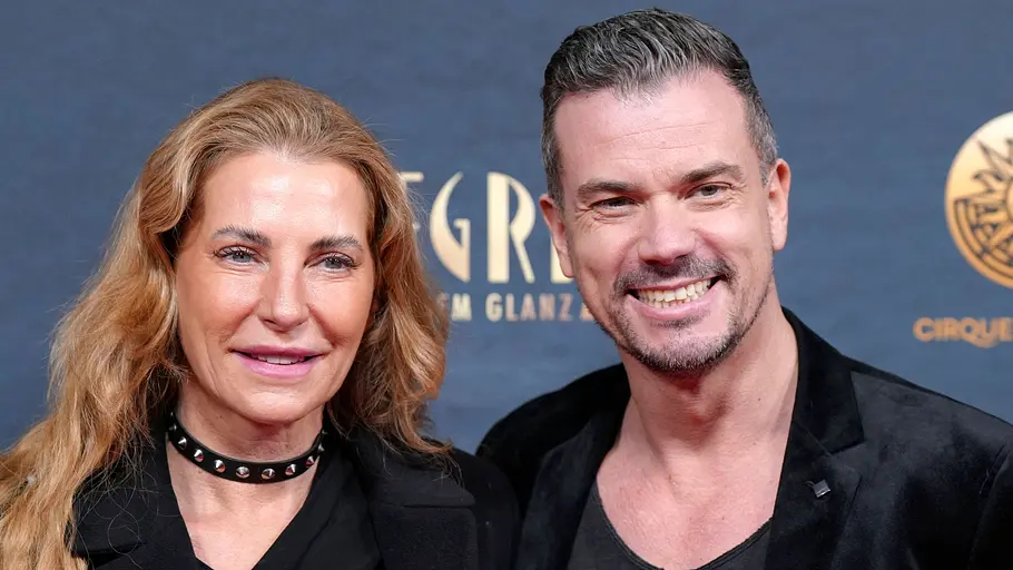 Giulia Siegel und Ludwig Heer Giulia Siegel und Ludwig Heer stehen lächelnd in schwarzer Kleidung vor einer blauen Wand mit goldenen Schriftzügen.