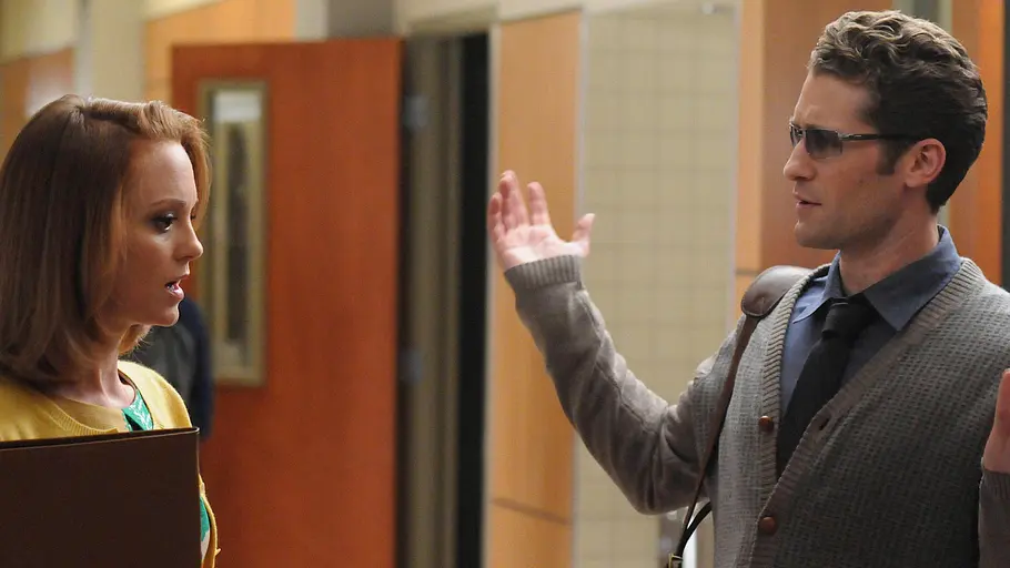 Glee Zwei Lehrkräfte unterhalten sich auf dem Flur einer Schule, während einer von ihnen gestikulierend die Hände hebt. Die Szene stammt aus der Musicalserie „Glee“.
