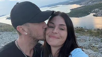 Gloria posiert mit ihrem Partner Micha bei Sonnenuntergang an einer Küste, während er ihr einen Kuss auf die Wange gibt. - Foto: Instagram: @gloriaschwesinger
