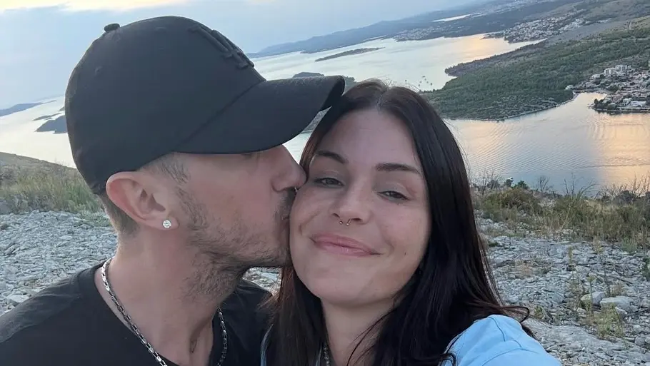Gloria & Micha: Alte Aufnahme des Reality-TV-Paares Gloria posiert mit ihrem Partner Micha bei Sonnenuntergang an einer Küste, während er ihr einen Kuss auf die Wange gibt.