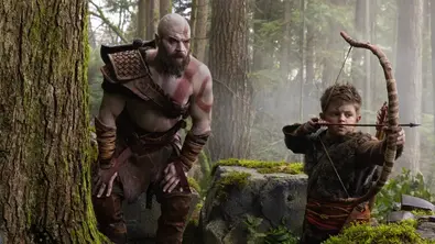 Kratos steht neben seinem Sohn und schaut ihm zu, wie er den Bogen spannt. - Foto: TMDB Kratos steht neben seinem Sohn und schaut ihm zu, wie er den Bogen spannt. - Foto: TMDB