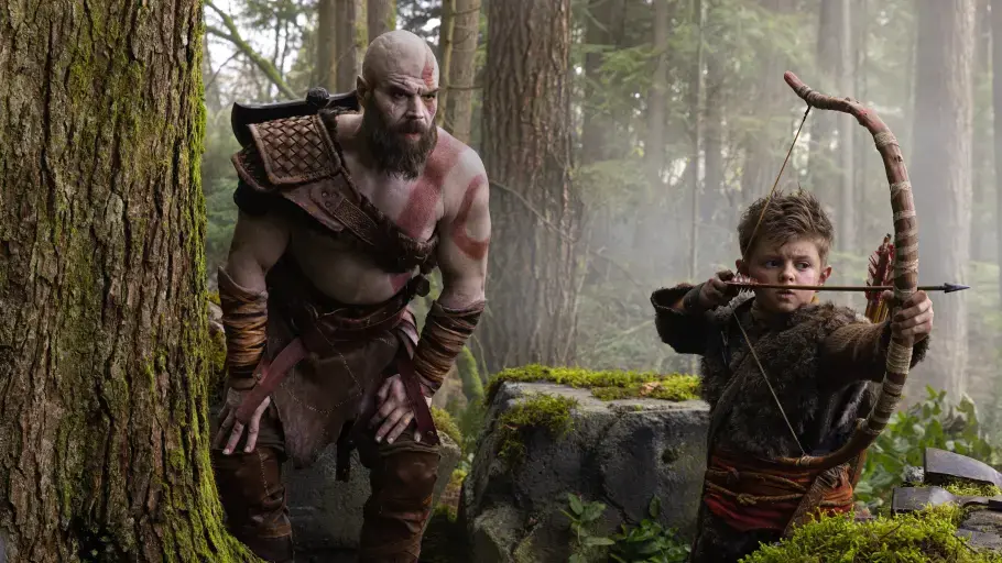 God of War - Serie Kratos steht neben seinem Sohn und schaut ihm zu, wie er den Bogen spannt.