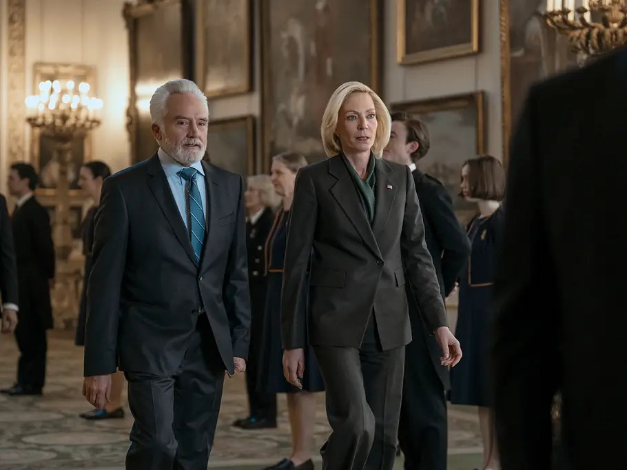 Grace verfolgt ihre eigenen Pläne und geht dabei taktisch äußerst klug vor. Bradley Whitford und Allison Janney gehen in dunklen Anzügen durch einen prunkvollen Saal mit Gemälden und weiteren Menschen.