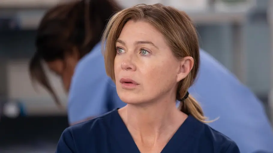 Greys Anatomy: Meredith sieht die neue Entwicklung kritisch Meredith trägt dunkelblaue OP-Kleidung und blickt nach links. Hinter ihr steht unscharf eine Person in hellblauer Kleidung.