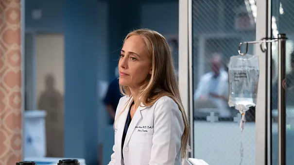 Eine Ärztin aus Greys Anatomy lehnt sich mit Kaffee in der Hand über ein Krankenbett - Foto: 2025 Disney. All rights reserved.