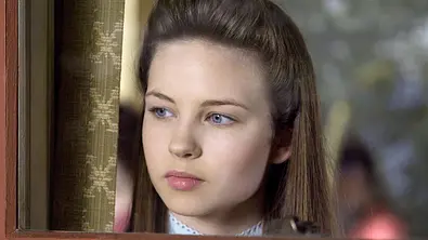 Daveigh Chase in der HBO-Serie Big Love, sie schaut aus dem Fenster. - Foto:  IMAGO / Everett Collection