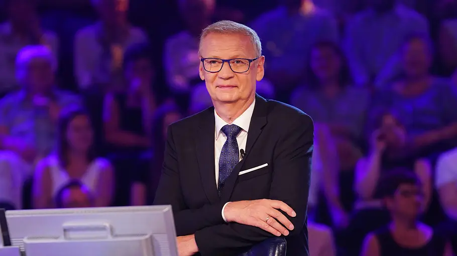 Günther Jauch Joker WWM Günther Jauch sitzt mit Brille, dunklem Anzug und Krawatte vor Monitoren. Im Hintergrund ist violett beleuchtetes Publikum.