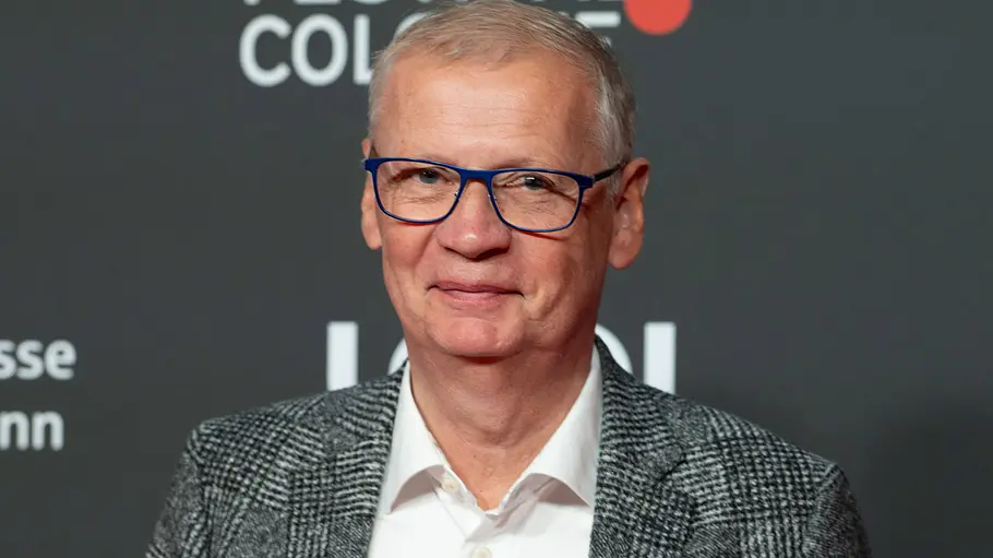 Günther Jauch Lets Dance Günther Jauch trägt eine blaue Brille, ein weißes Hemd und ein grau kariertes Sakko vor einer dunklen Festivalwand.