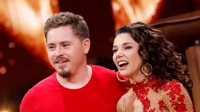 Gustav Schäfer und seine Tanzpartnerin Anastasia Maruster stehen lachend nebeneinander auf dem „Let’s Dance“-Parkett in roten Outfits - Foto: IMAGO / Panama Pictures