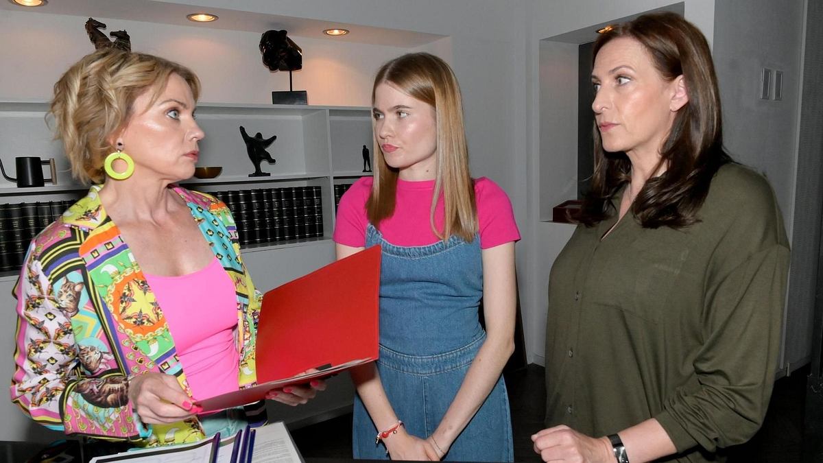 GZSZ-Szene: Yvonne steht mit Johanna und Katrin zusammen. Sie hält eine rote Mappe in der Hand. Alle sehen besorgt aus.