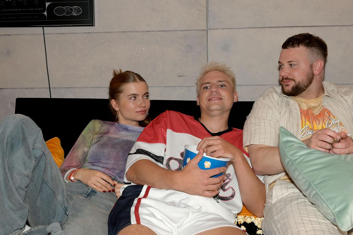 GZSZ-Szene: Johanna, Moritz und Jonas sitzen zusammen auf dem Sofa, Jonas und Johanna schauen sich verliebt an