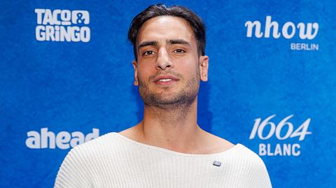 GZSZ-Star Timur Ülker posiert ganz in Weißgekleidet vor einer Fotowand - Foto:  IMAGO / Eventpress