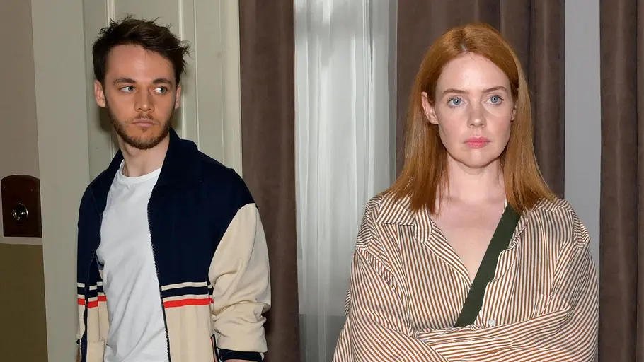 Toni und Robin sind Halbgeschwister oder etwa doch nicht? Robin schaut Toni ernst an, die verschränkt ihre Arme.