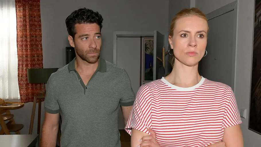 Zoe geht ihrem alten Job nach. Zoe schaut ernst mit verschränkten Armen, hinter ihr Carlos.