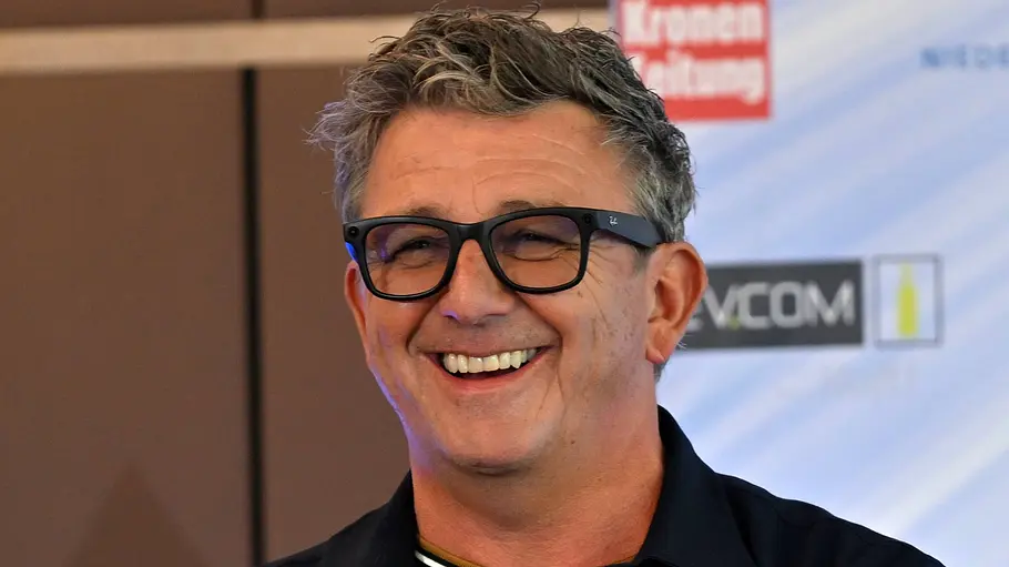 Hans Sigl Hans Sigl lächelt mit schwarzer Brille und dunklem Hemd vor einer Wand mit Logos. Sein kurzes Haar ist grau meliert.