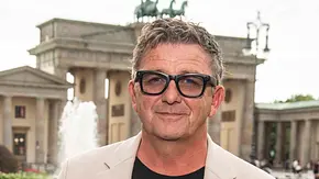 Hans Sigl steht vor dem Brandenburger Tor mit Sonnenbrille und lächelt. - Foto: IMAGO / BREUEL-BILD Hans Sigl steht vor dem Brandenburger Tor mit Sonnenbrille und lächelt. - Foto: IMAGO / BREUEL-BILD