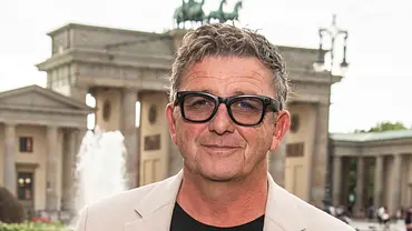 Hans Sigl steht vor dem Brandenburger Tor mit Sonnenbrille und lächelt. - Foto: IMAGO / BREUEL-BILD Hans Sigl steht vor dem Brandenburger Tor mit Sonnenbrille und lächelt. - Foto: IMAGO / BREUEL-BILD