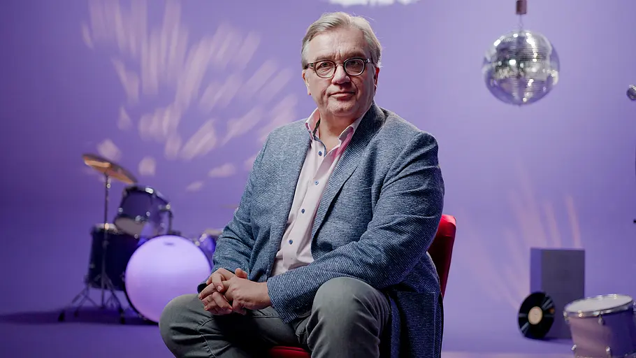 Hape Kerkeling glaubt an den ESC, aber nicht an den Sieg von Deutschland. Hape Kerkeling im Interview, hinter ihm ein Schlagzeug und eine Discokugel.