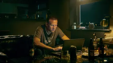 Detektiv Harry Hole sitzt in T-Shirt an seinem Schreibtisch und schaut gebannt auf seinen Laptop - Foto: Netflix