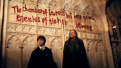 Harry Potter und Finch stehen vor einer Wand. Auf dieser steht eine Nachricht in Blut geschrieben. - Foto: Warner Bros.