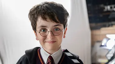 Dominic McLaughlin spielt Harry Potter und steht im typischen Potter-Outfit mit einer Filmklappe in der Hand - Foto: HBO