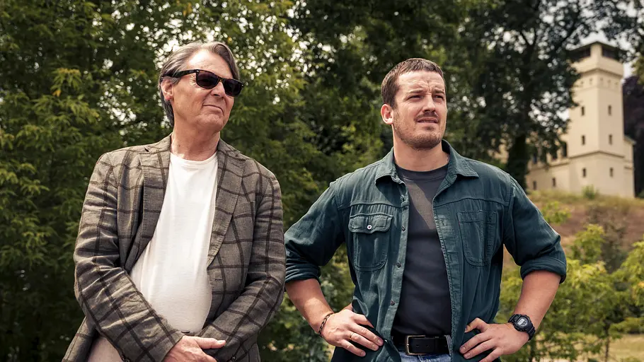 Ausschnitt: Armin (Wolfgang Bahro, l.) und Gregor (Felix Kreutzer) stehen nebeneinander. Wolfgang Bahro trägt eine Sonnenbrille.  