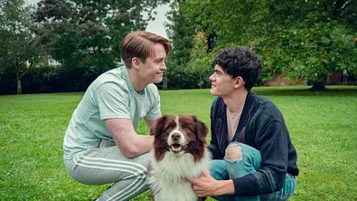 Zwei Cast-Member gehen in die Hocke. Zwischen ihnen sitzt Hund Echo. - Foto: Samuel Dore/Netflix