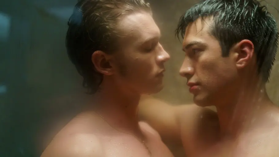 Ilya und Shane stehen sich nackt und eng in einer dampfenden Dusche gegenüber. Sie schauen sich intensiv in die Augen, der Moment wirkt sehr intim und emotional. Das Licht ist weich und die Scheibe leicht beschlagen.