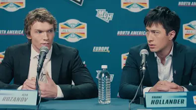 Die Serie „Heated Rivalry“ ist Teil des HBO-Portfolios. Das Foto zeigt zwei Charaktere, die Anzüge tragen und mit ernsten Gesichtsausdrücken Fragen bei einer Pressekonferenz beantworten. - Foto: Crave / HBO Max