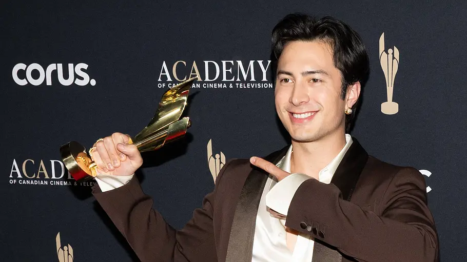 Hudson Williams lächelt bei einer Preisverleihung und hält eine goldene Trophäe hoch.